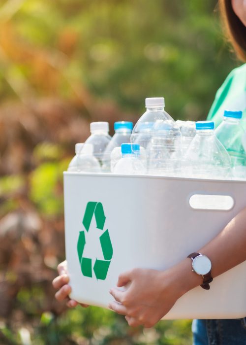 A beautiful asian woman collecting garbage and holding a recycle bin with plastic bottles in the outdoors